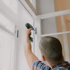 Mężczyzna z wkrętarką montuje białe okno.