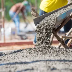 Beton wylewany z rynny na placu budowy, w tle pracownicy.