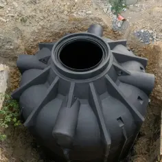Czarny plastikowy szambo w wykopie ziemnym, gotowe do montażu.