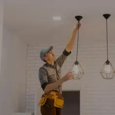 Elektryk montuje lampę wiszącą na suficie.