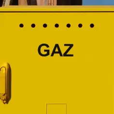Żółta skrzynka gazowa z napisem "GAZ" na tle budowy.