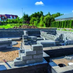 Budowa fundamentów domu z bloczków betonowych, widoczne zbrojenie i piasek.