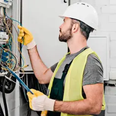 Elektryk w kasku i kamizelce odblaskowej pracuje przy skrzynce z przewodami.