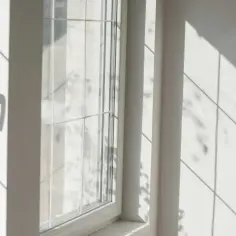 Jasne, białe okno balkonowe w bloku, z widocznym uchwytem. Słońce rzuca ciekawe cienie. Zastanawiasz się, ile kosztuje wymiana okna balkonowego w bloku?