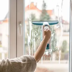 Kobieta myje okno elektryczną myjką, na szybie widać pianę.