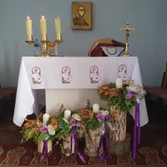 Ołtarz kościelny ozdobiony na Adwent: świece, kwiaty, krzyż i księga.