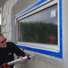 Mężczyzna z pistoletem na masę uszczelniającą zabezpiecza piankę przy nowym oknie.