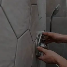 Dłonie montują chromowaną baterię podtynkową w łazience z geometrycznymi płytkami.