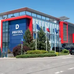 Nowoczesny budynek firmy Drutex w Bytowie z flagami i zielenią.