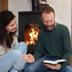 Para siedząca przy kominku na ekogroszek, czytająca książkę.