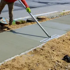 Robotnik wygładza świeży beton na budowie chodnika za pomocą kielni.
